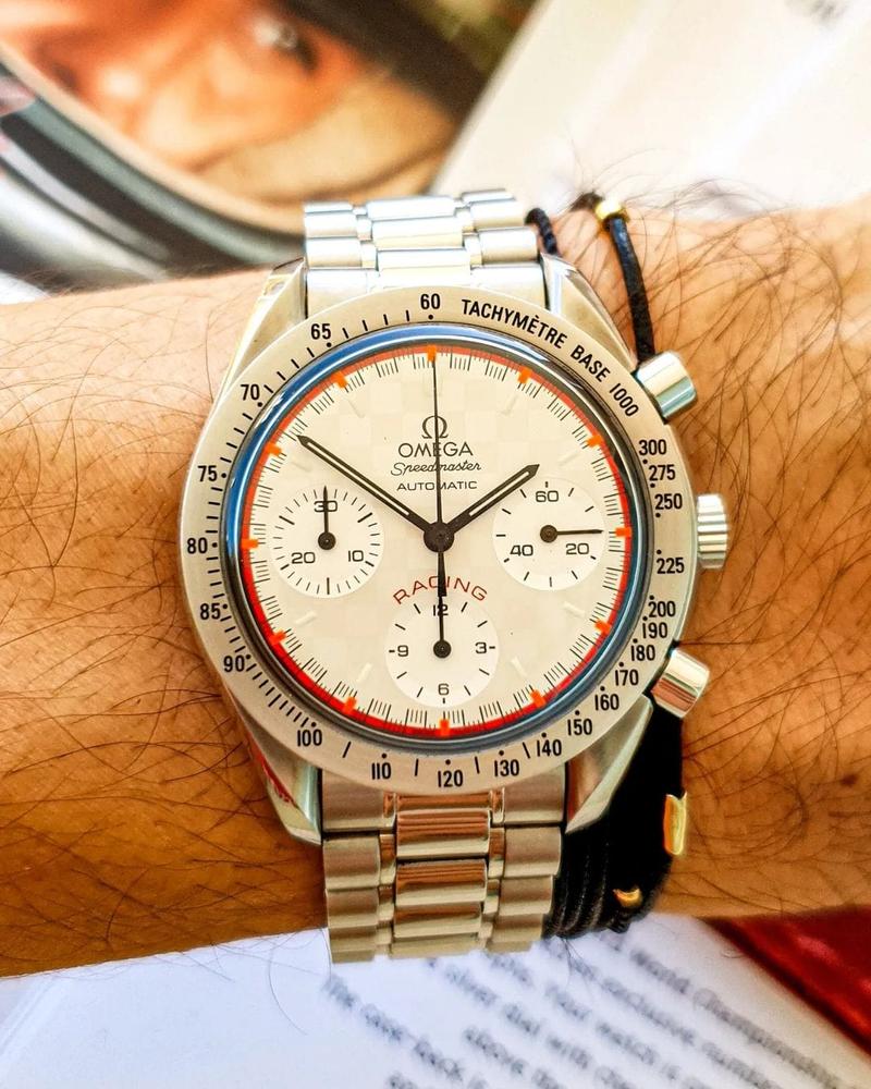 Schumacher light dial with “Racing” print and checkered pattern. Orange and red outer ring along the seconds track. Black hands. Painted indices with luminescent material. Omega Speedmaster Reduced 3517.30.00